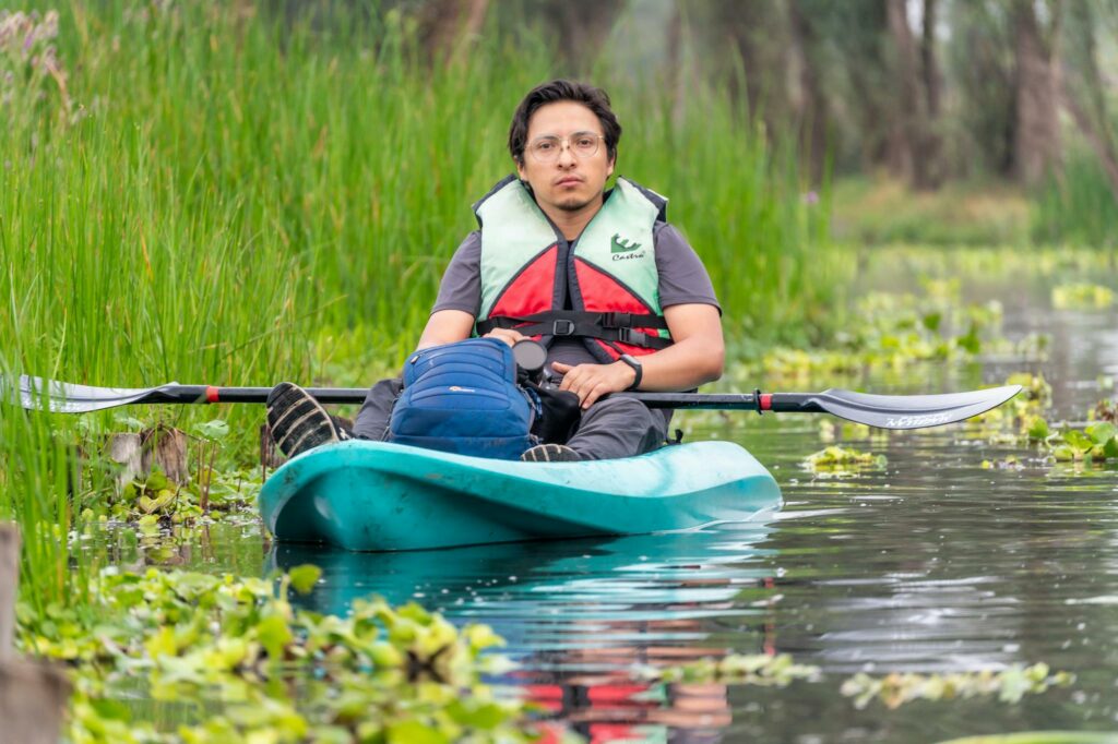 A woman in a life jacket paddles a kayak through a swamp