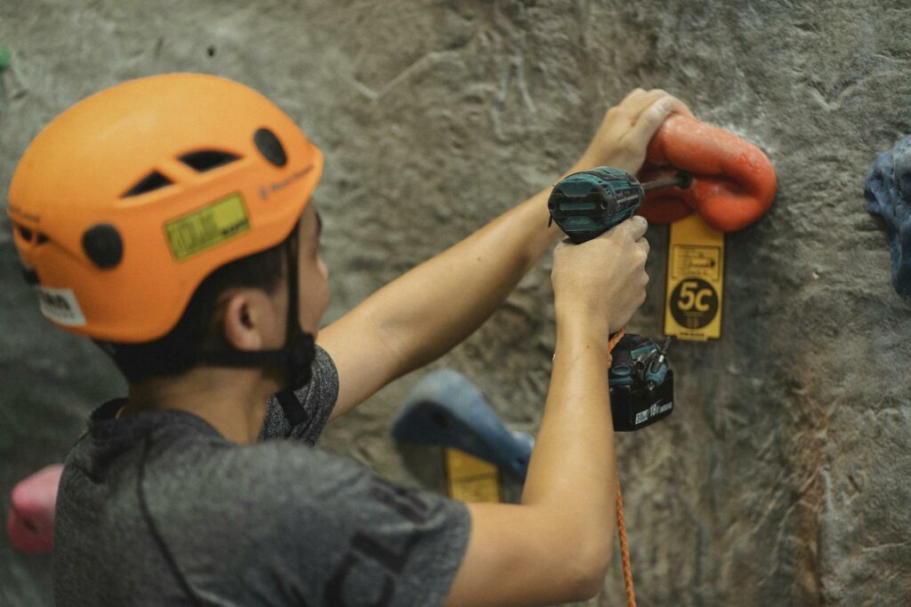 Crop athlete fasten climbing hold with screwdriver on wall in gym